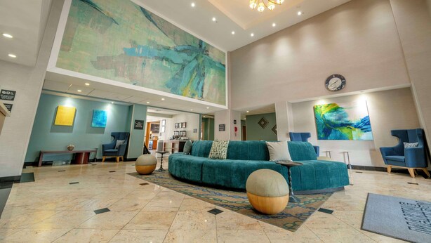 A spacious lobby with a large abstract painting, a modern chandelier, and a seating area with a teal sofa and armchairs.