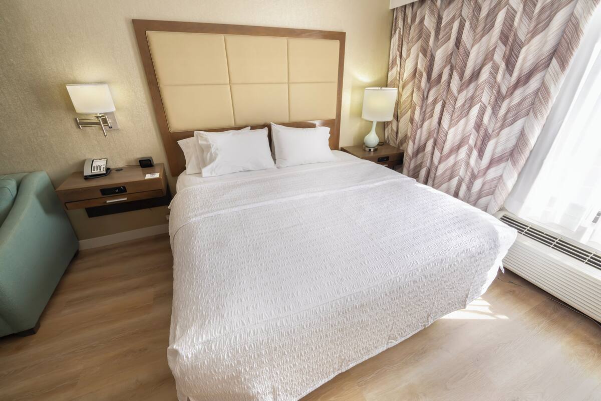 Une chambre d’hôtel avec un grand lit, deux tables de chevet avec des lampes, un téléphone et un radiateur fixé au mur.
