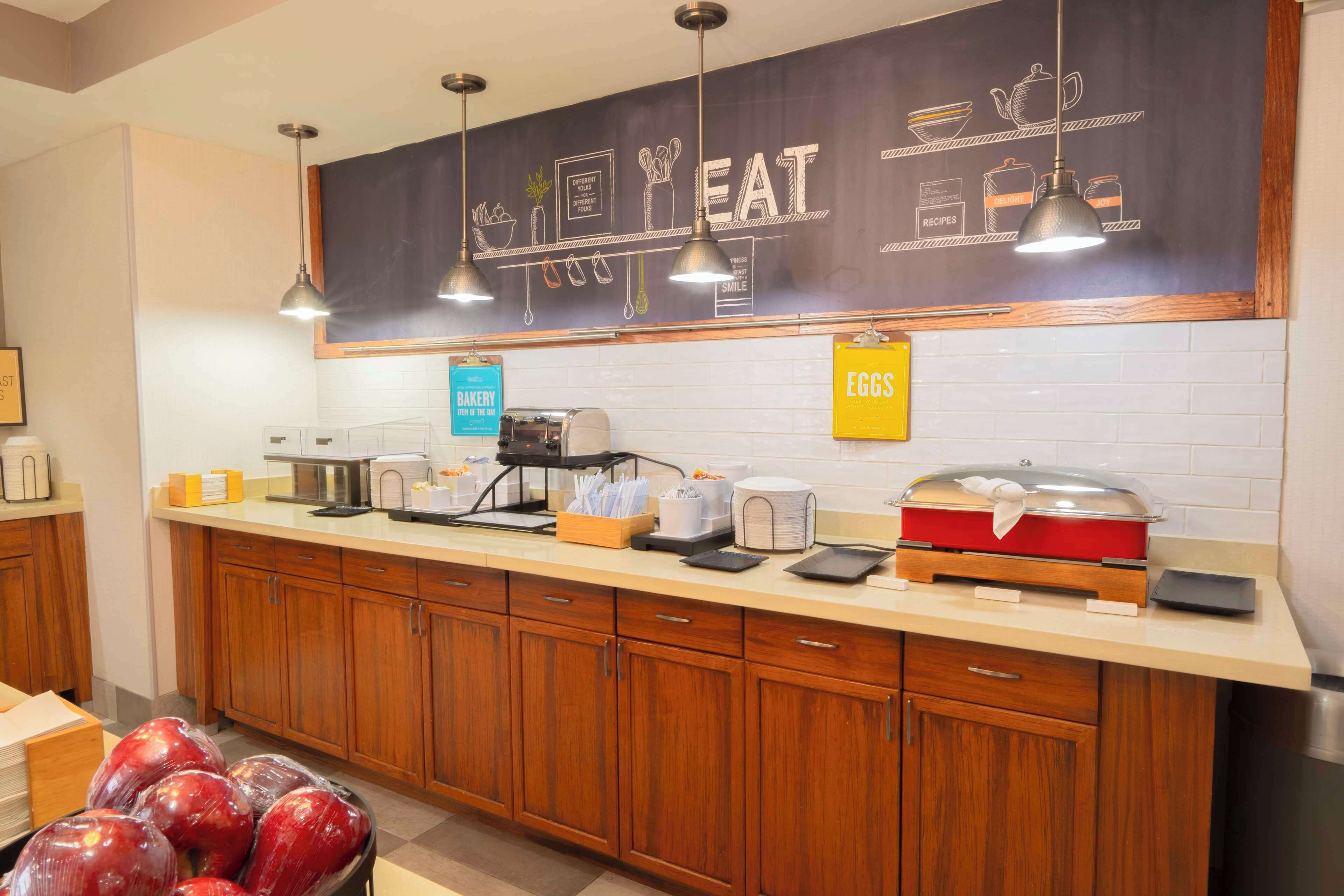 A kitchen area with wooden cabinets, a chalkboard menu, and various kitchen appliances.