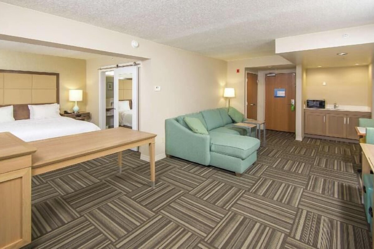 Una habitación de hotel con cama, escritorio, sofá, kitchenette y baño.