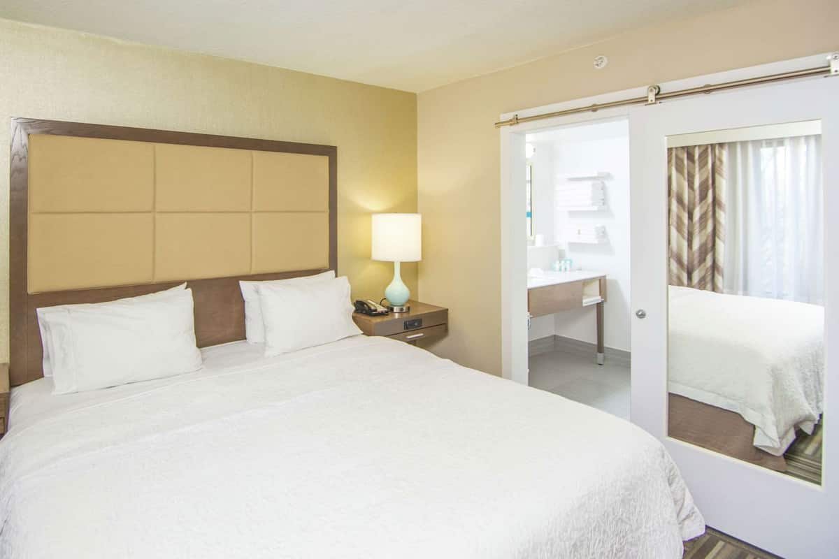Une chambre d’hôtel avec un grand lit, une lampe de chevet, une table de chevet, un miroir et une porte donnant accès à une salle de bain.