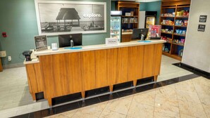 A hotel reception area with a wooden counter, a large 'explore.' poster, a minibar, and a snack shelf.