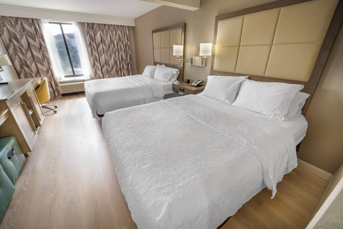 Une chambre d’hôtel avec deux lits, un bureau, une chaise et une grande fenêtre.