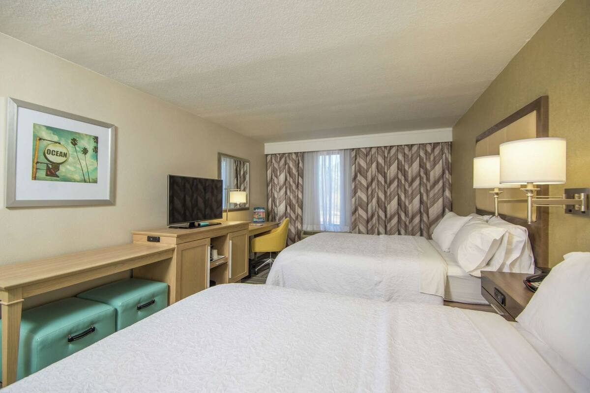 Une chambre d’hôtel avec deux lits, un bureau, une télévision, une chaise et un tableau au mur.
