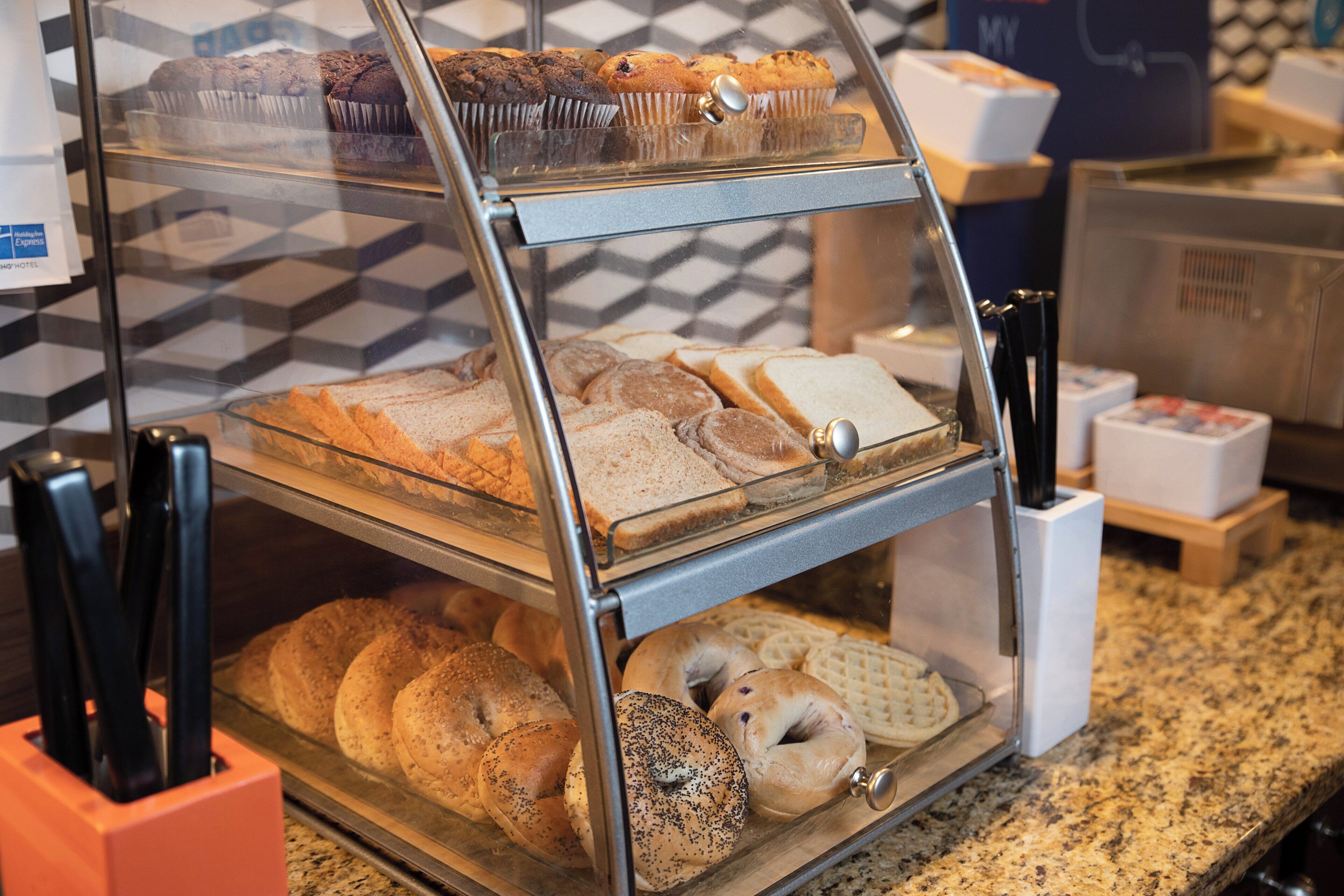 A bakery display case with various baked goods including muffins, bread, and bagels.