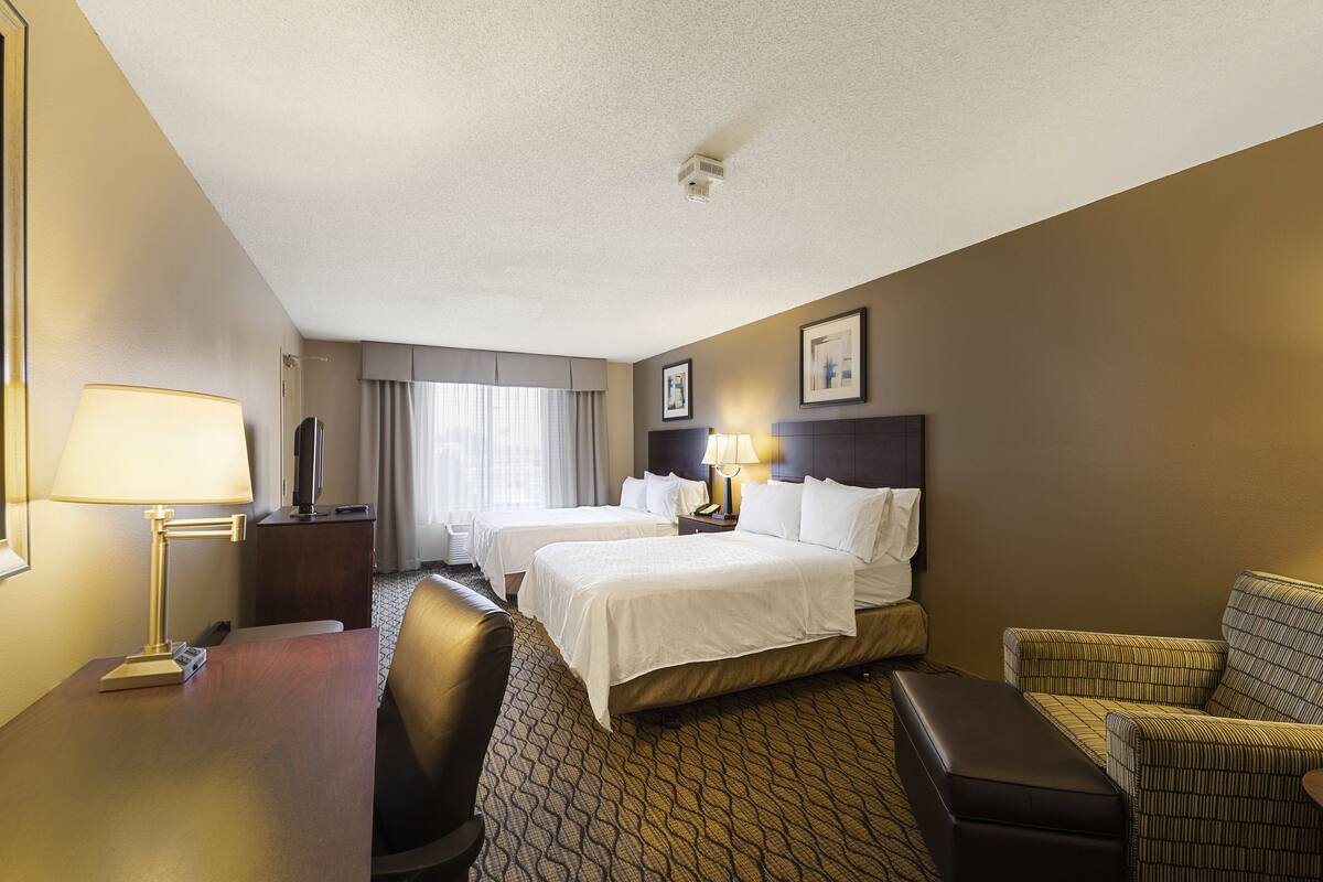 A hotel room with two beds, a desk, a chair, and a sofa.