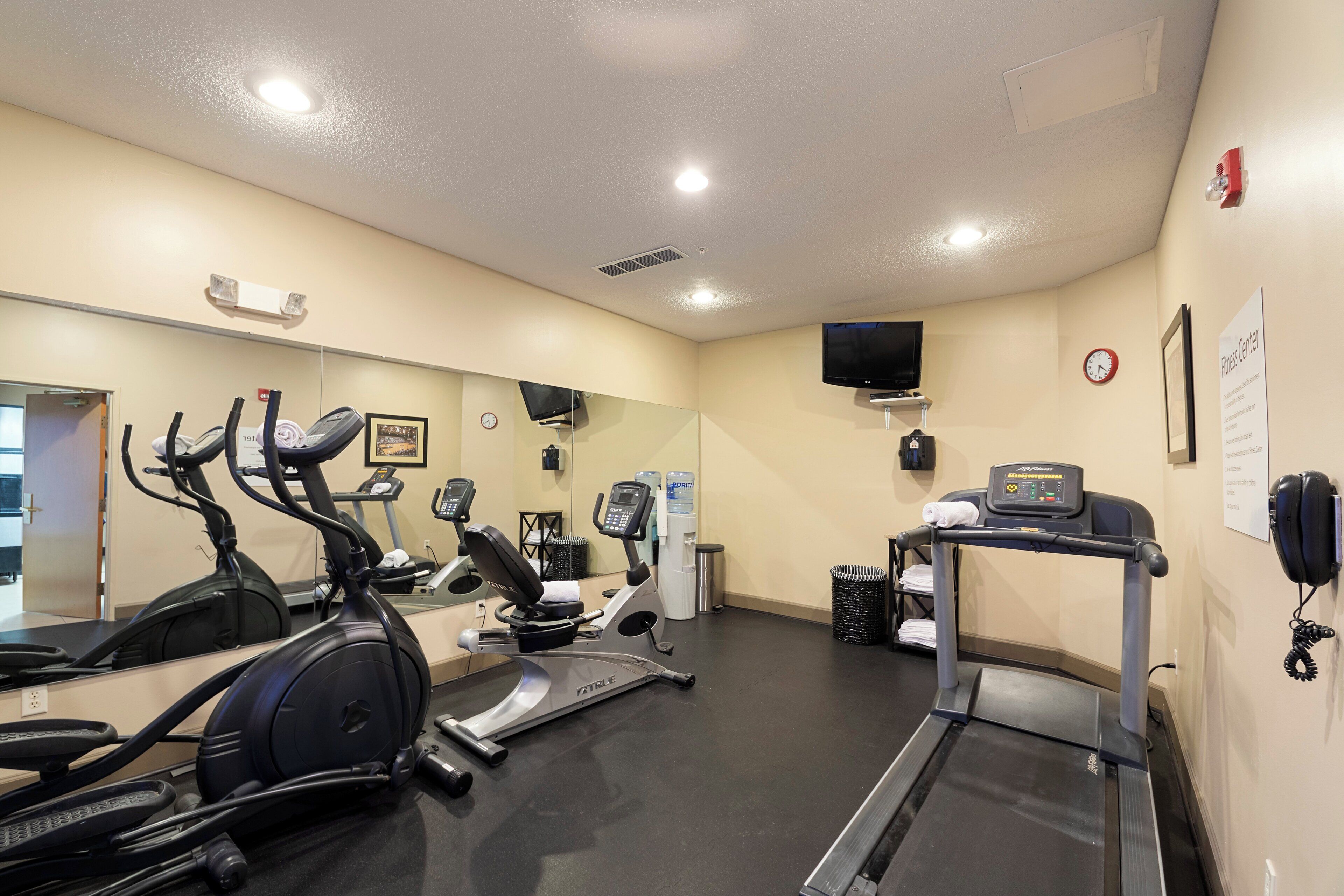 A gym with various exercise equipment, a water dispenser, a clock, and a television on the wall.