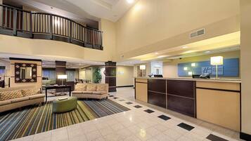 A hotel lobby with a reception desk, seating area, and a staircase.