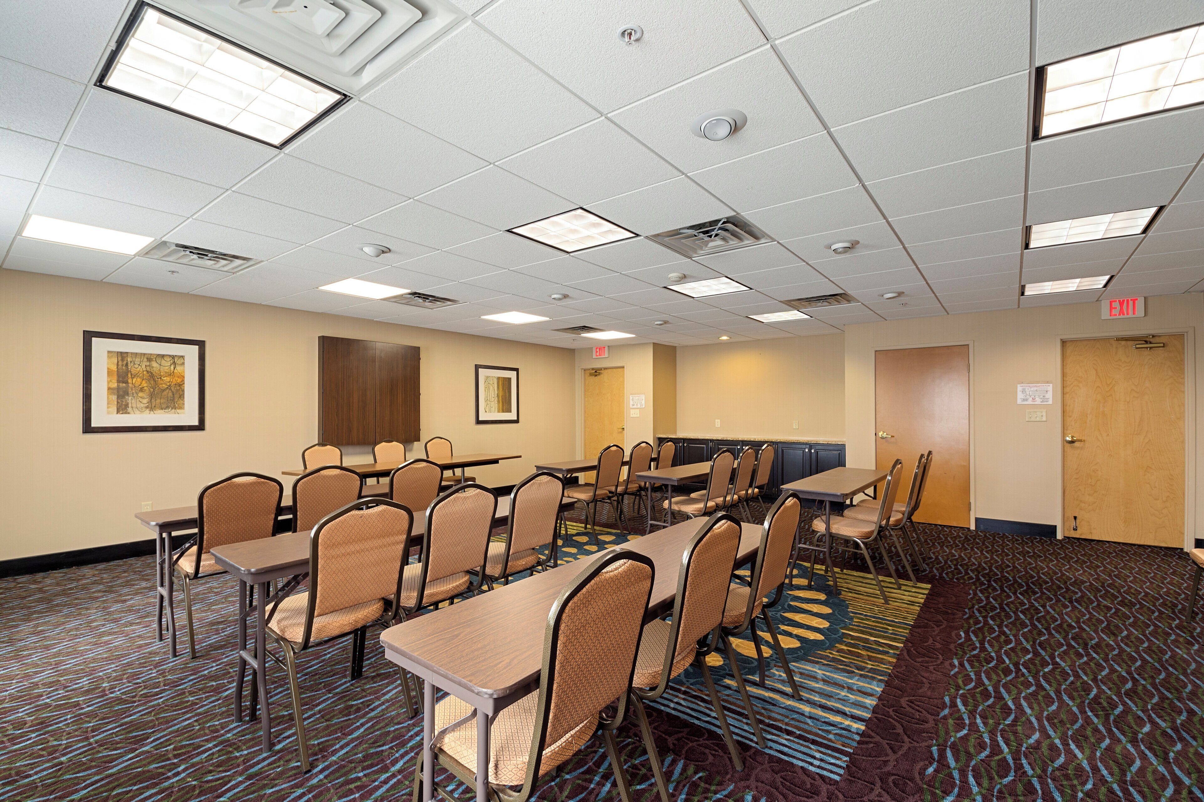 A conference room with multiple tables and chairs, a patterned carpet, and a ceiling with recessed lighting.