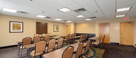 A conference room with multiple tables and chairs, a patterned carpet, and a ceiling with recessed lighting.