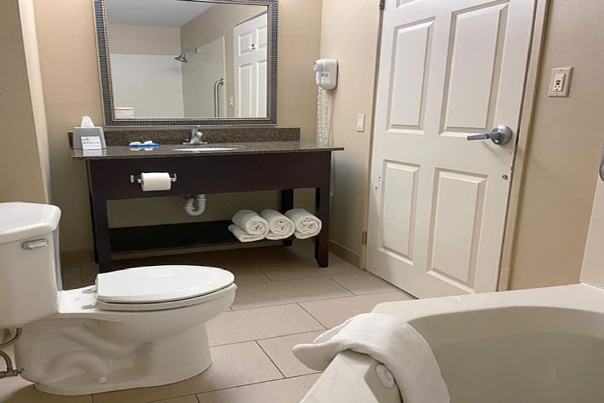 A bathroom with a toilet, sink, mirror, and bathtub.