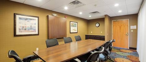 A conference room with a long table, six chairs, two framed pictures on the wall, a clock, and a door.