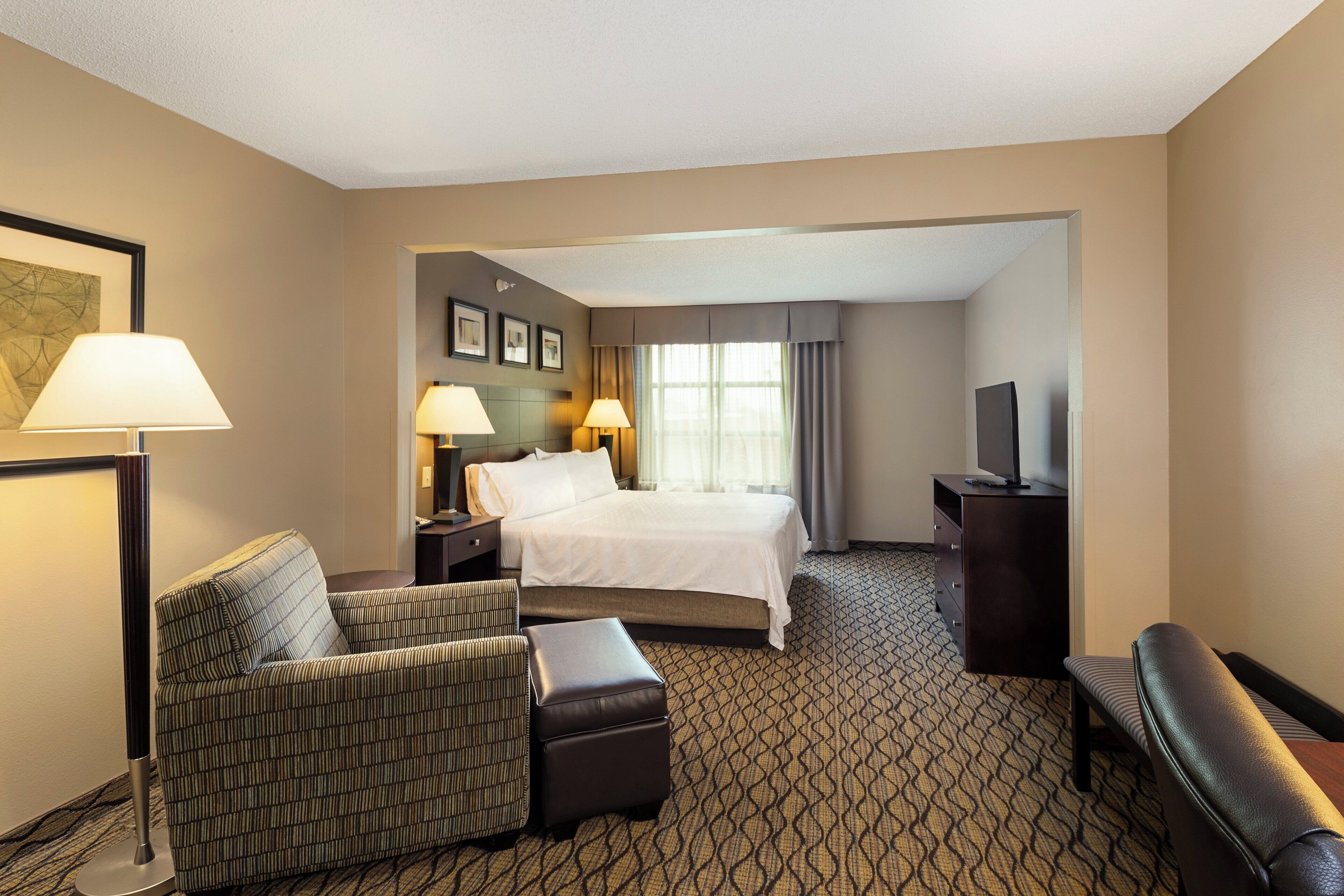 A hotel room with a bed, two bedside tables with lamps, a television, a sofa, a chair, and a patterned carpet.