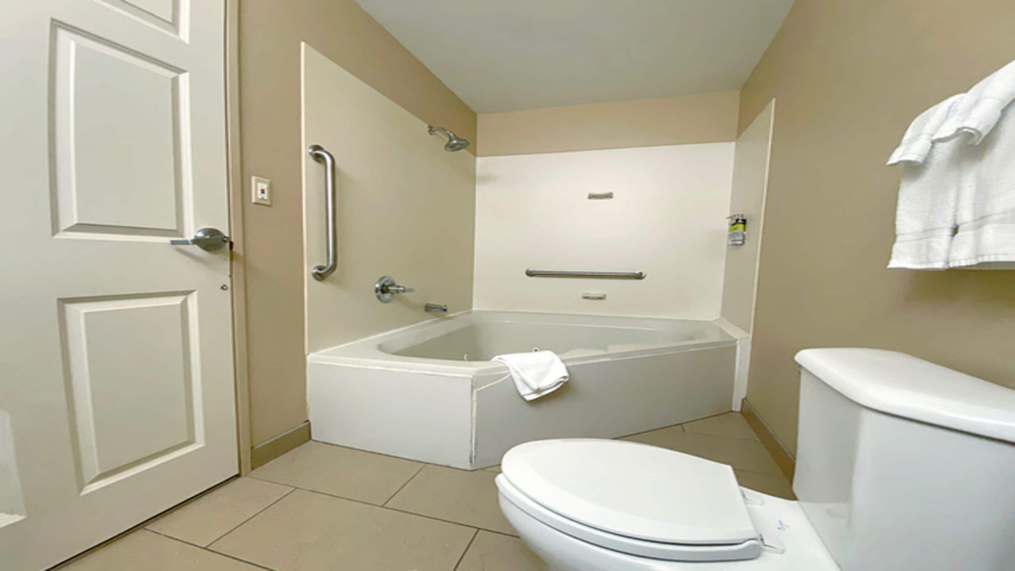 Un baño con bañera, inodoro y barras de apoyo.