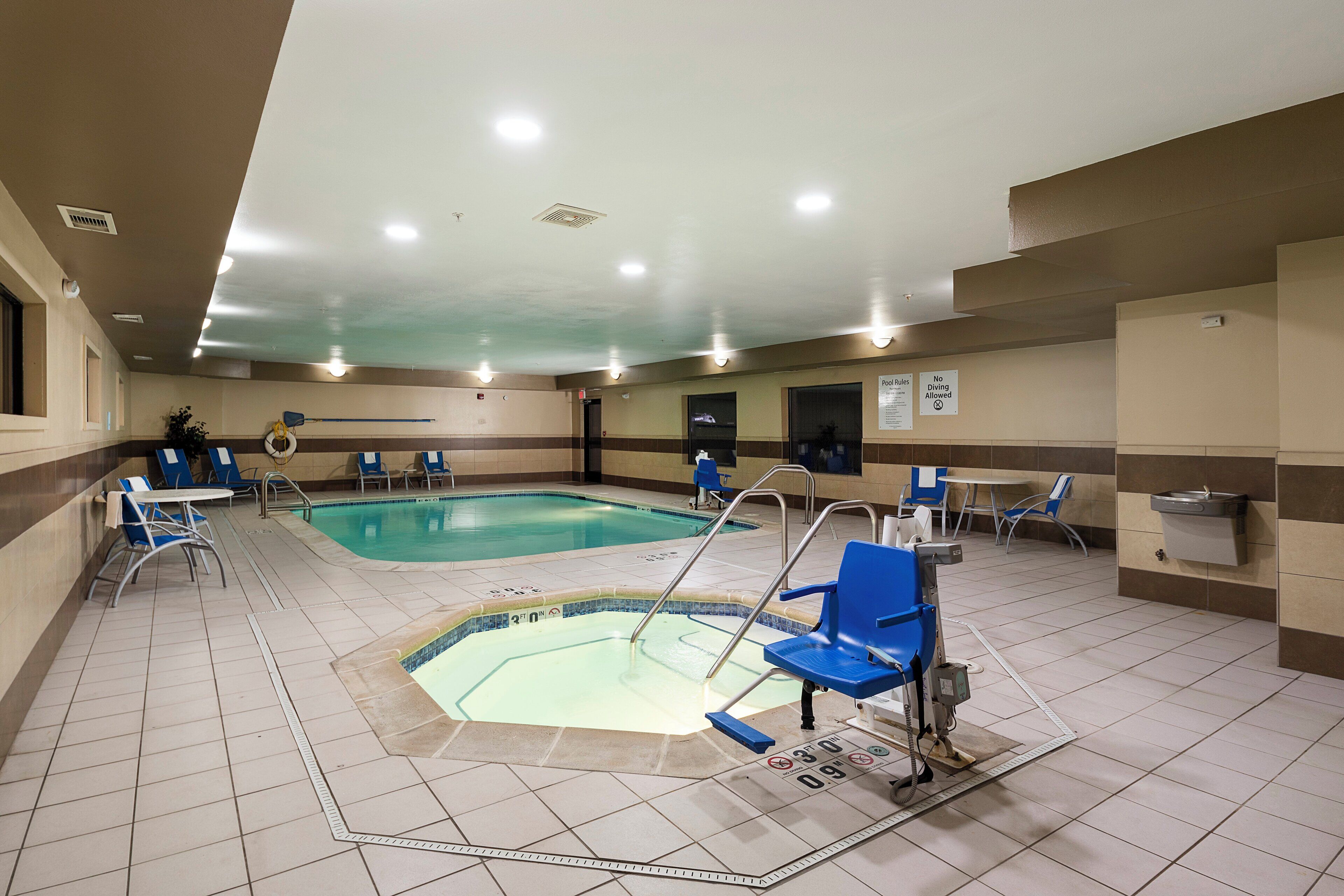 An indoor swimming pool with multiple lanes, blue chairs, and a lifeguard chair.