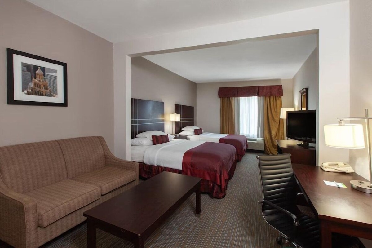 A hotel room with a sofa, a desk, two beds, a TV, and a framed picture on the wall.