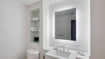 A modern bathroom with a toilet, a sink, a mirror, and a glass shelf with towels.