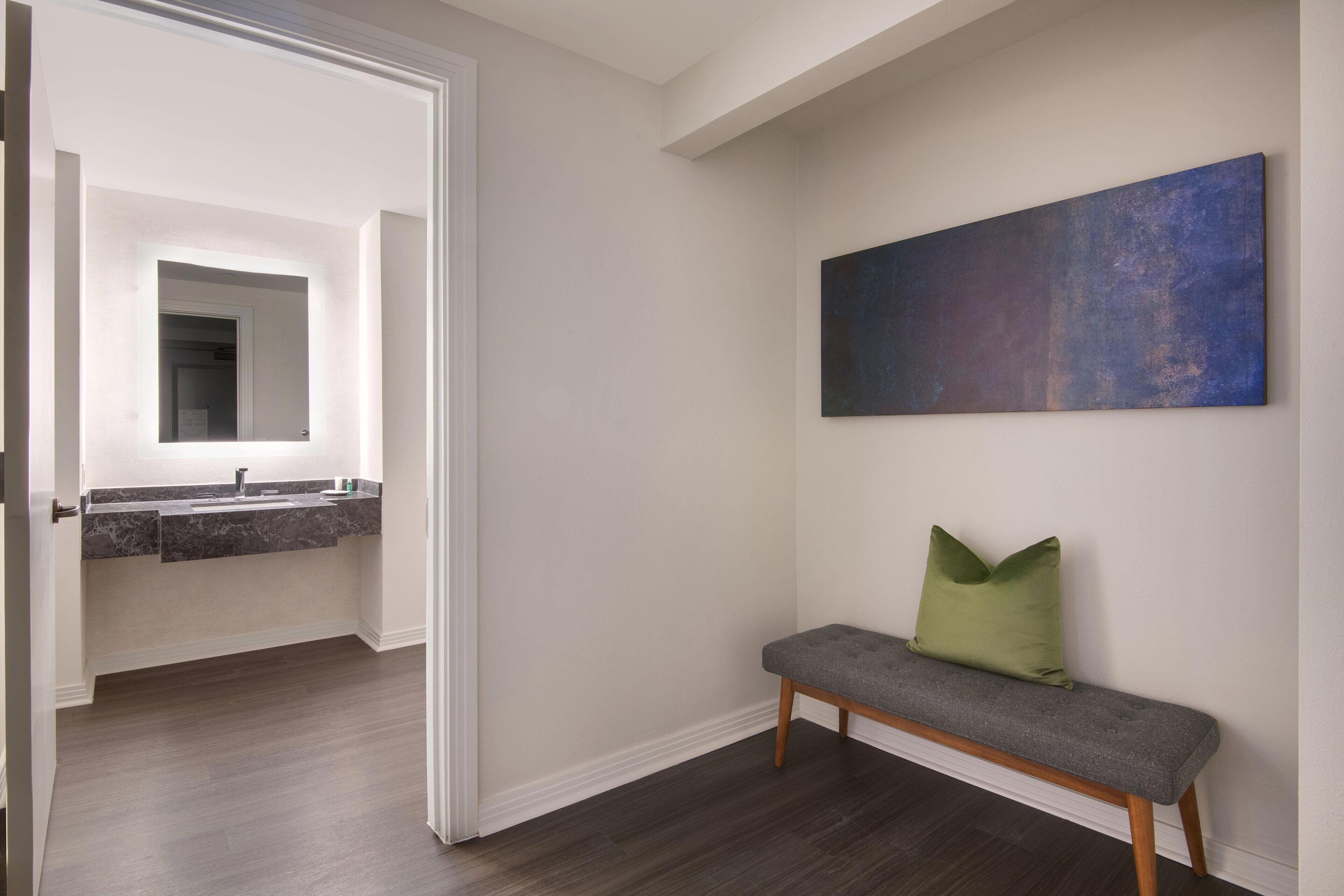 A hallway with a bench, a painting on the wall, and a bathroom visible through an open door.