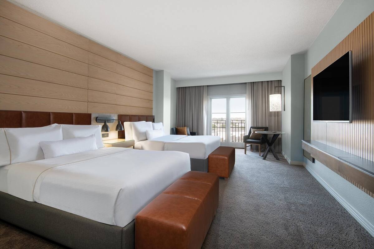 A hotel room with two beds, a sofa, a TV, and a balcony with curtains.