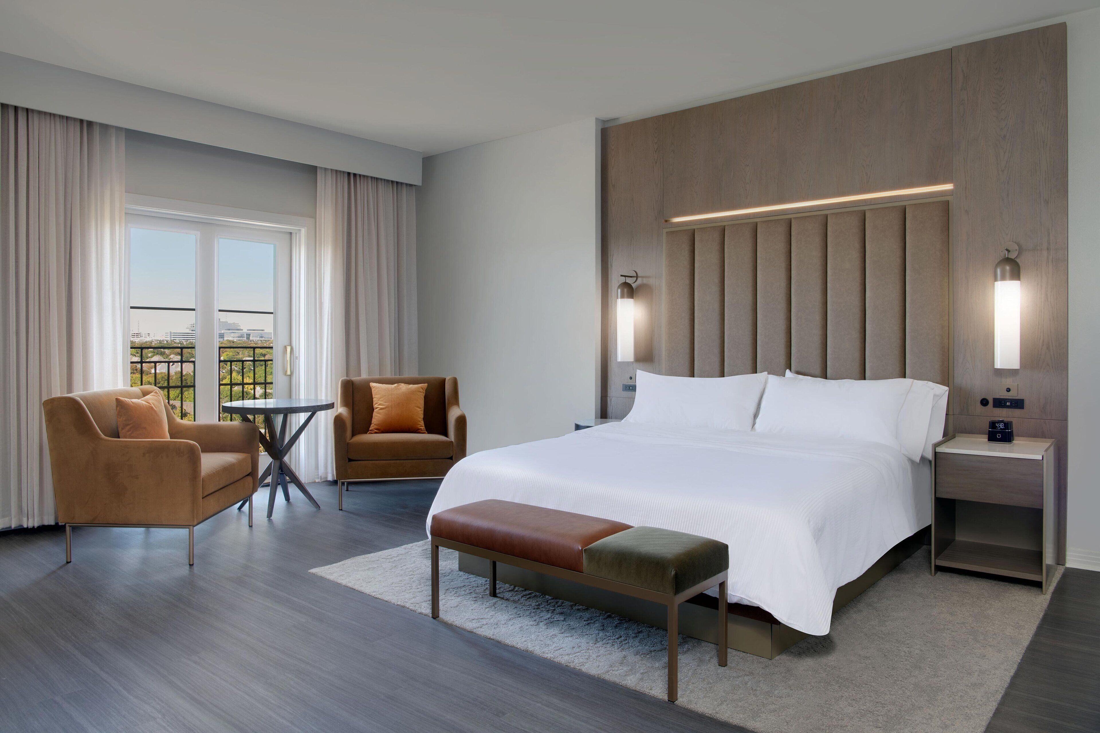 Et moderne hotelværelse med en stor seng, et siddeområde med sofa og lænestol, et lille bord og en bænk.