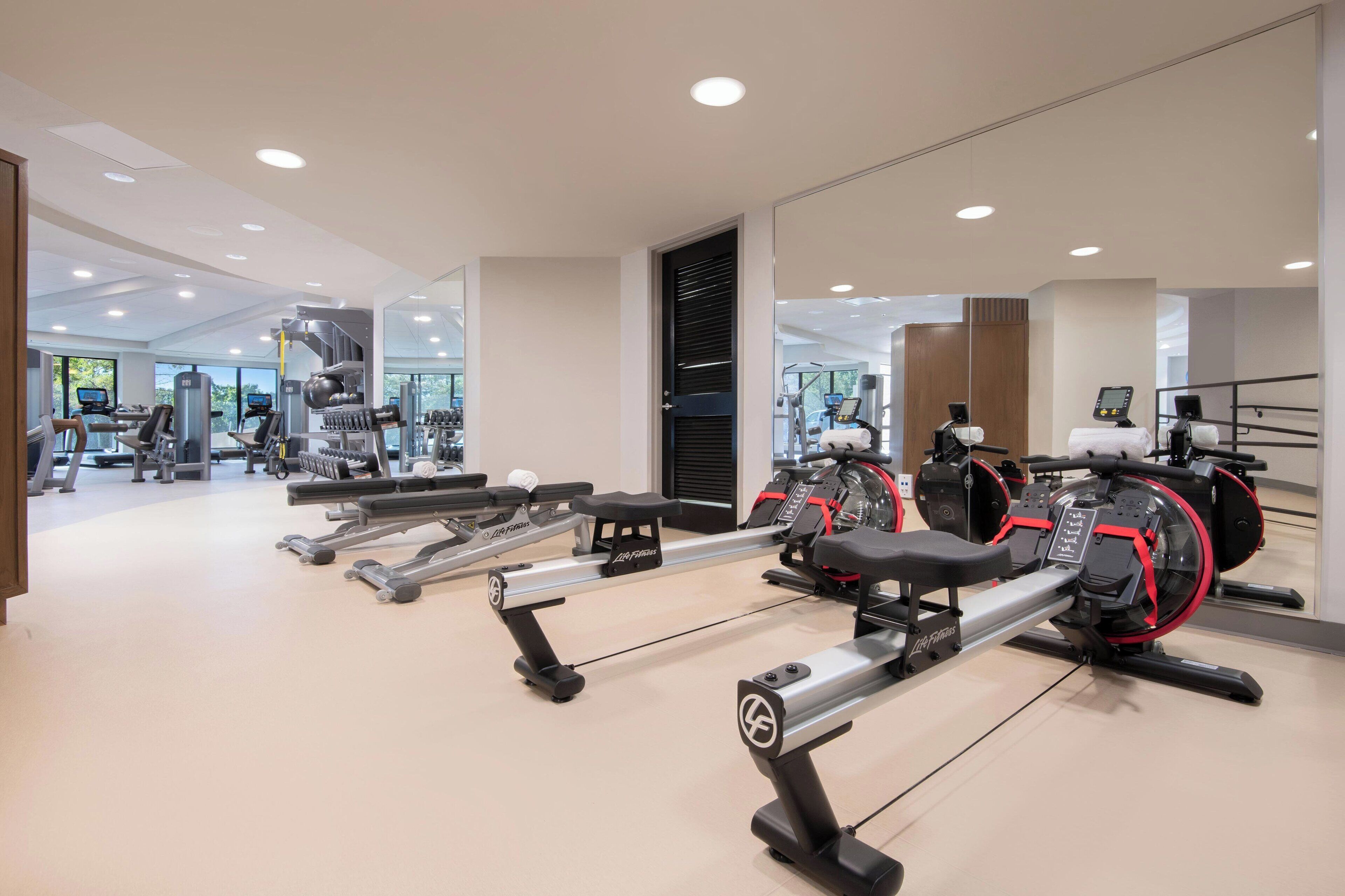 A modern gym with rowing machines, weight benches, and various cardio equipment.