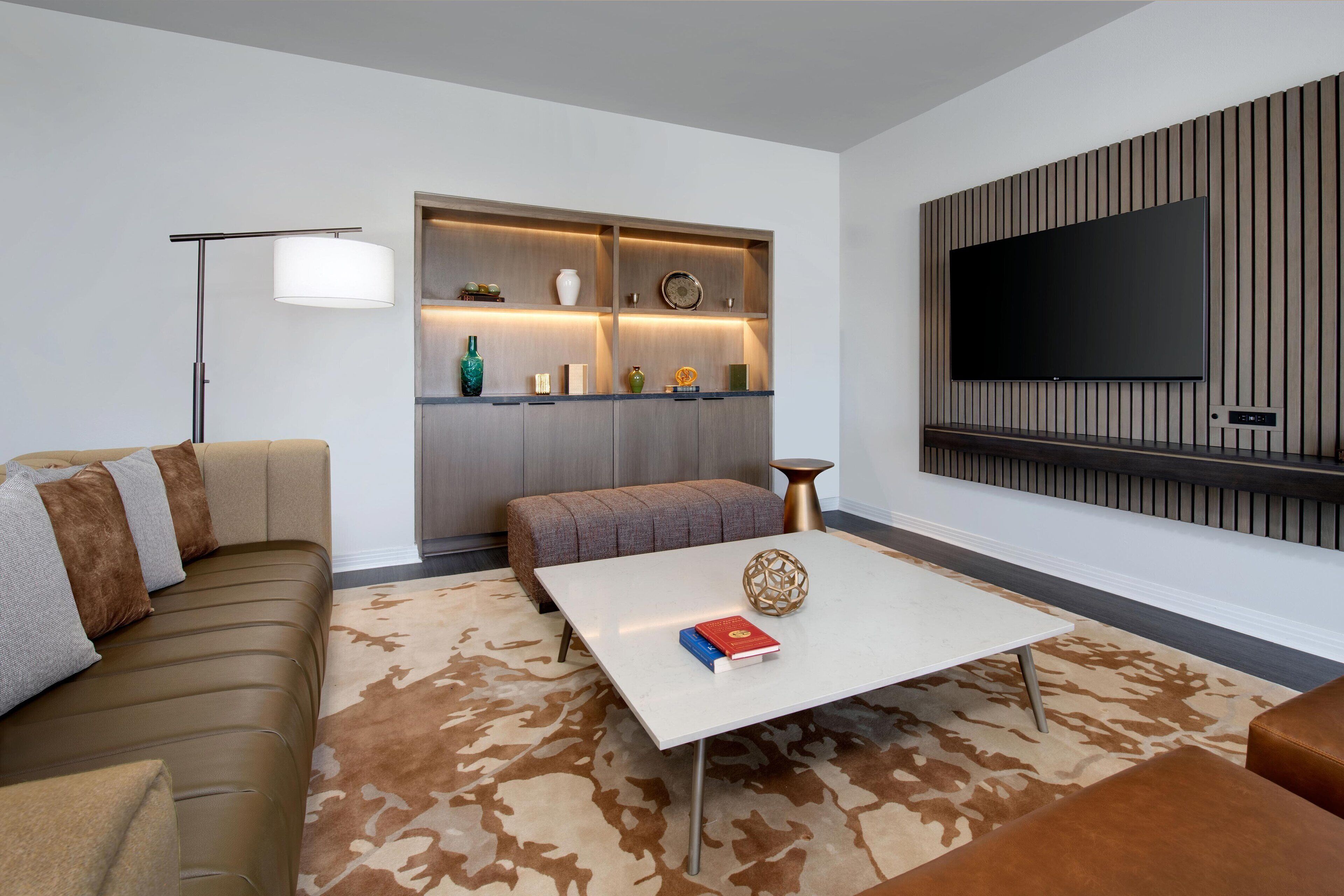 Una sala de estar moderna con un sofá, una mesa de centro, un mueble de pared para televisión y un estante empotrado con objetos decorativos.