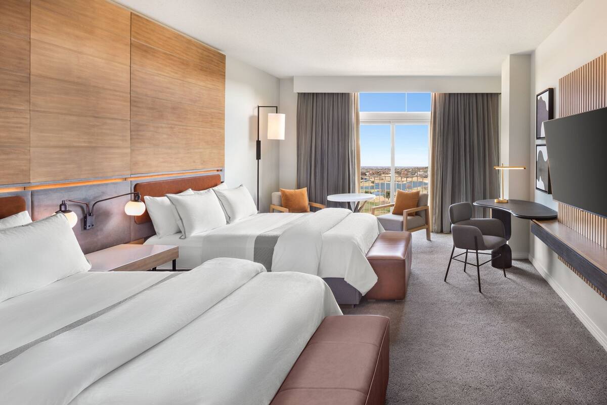 A hotel room with two beds, a desk, a chair, and a TV.