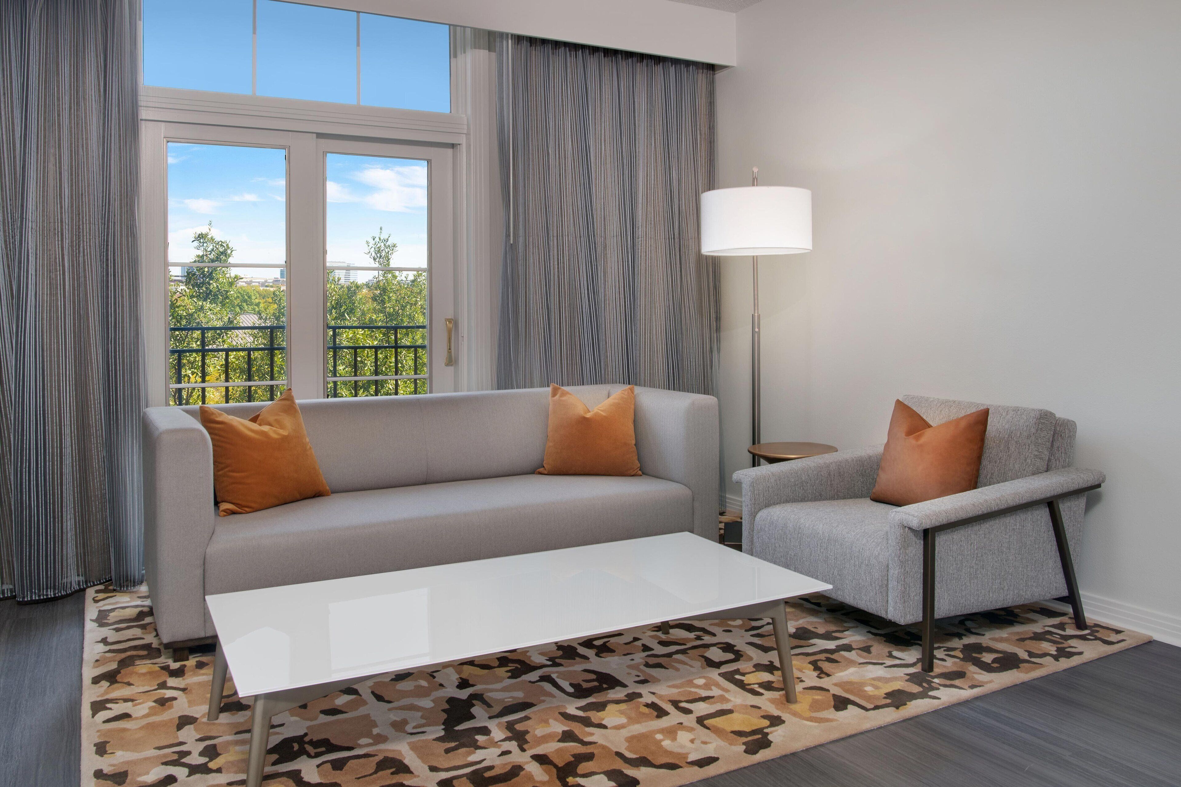 A modern living room with a grey sofa, a matching armchair, a white coffee table, and a patterned rug.