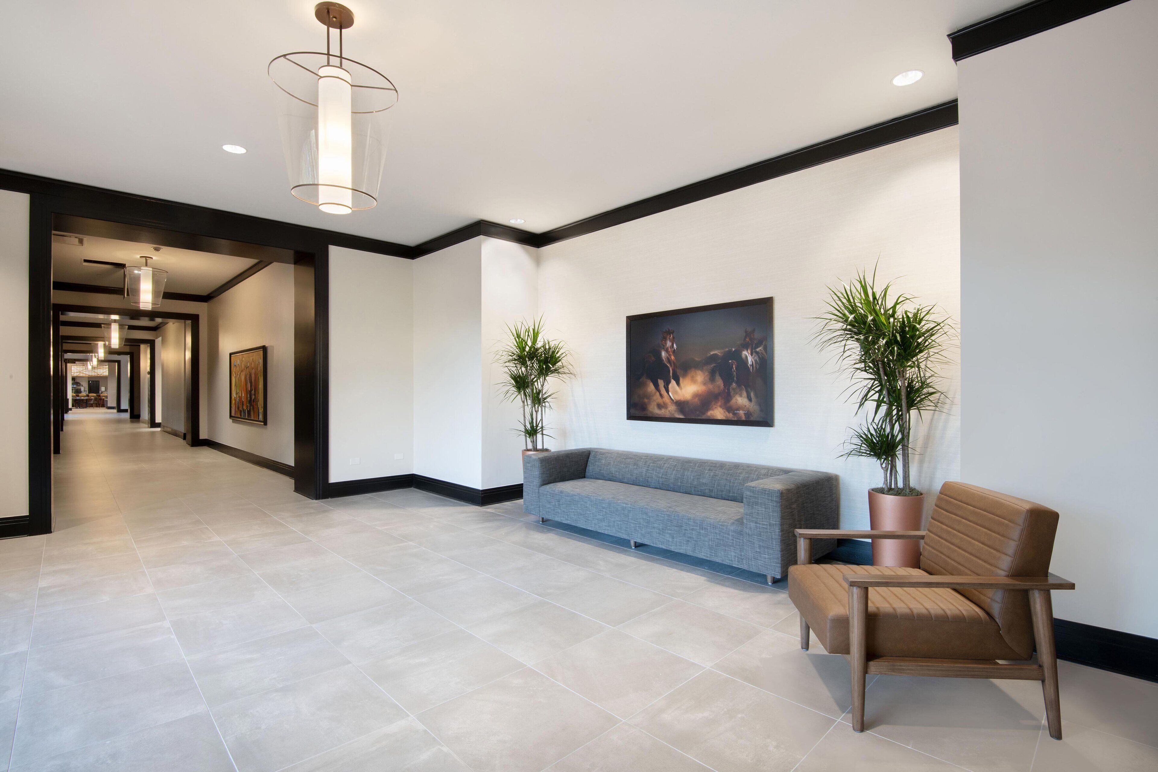 A modern lobby with a grey sofa, a wooden chair, and two potted plants.