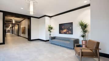 A modern lobby with a grey sofa, a wooden chair, and two potted plants.