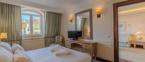 A hotel room with a bed, a desk with a television, a mirror, and a view of the outside.