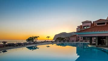 Une piscine d’hôtel avec des chaises longues, un ciel dégagé et une montagne en arrière-plan.