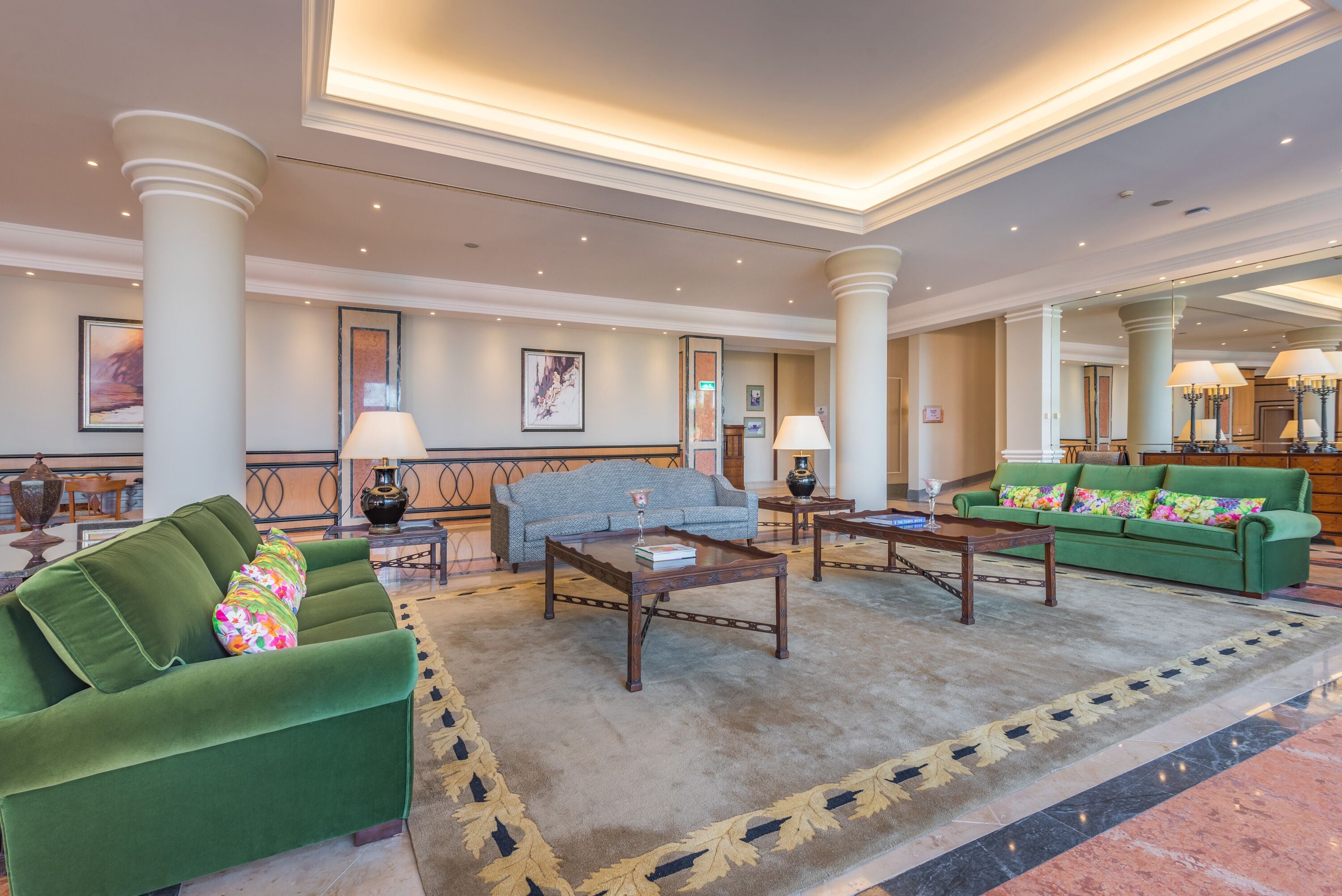 A spacious lobby with a green sofa, a blue sofa, and a wooden coffee table.