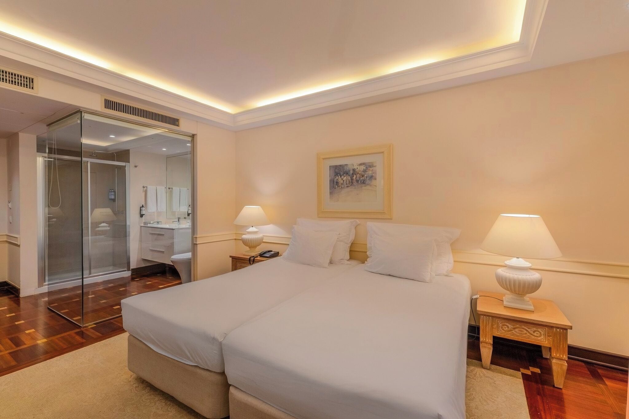 A hotel room with a large bed, bedside lamps, a painting on the wall, and a glass-enclosed shower area.