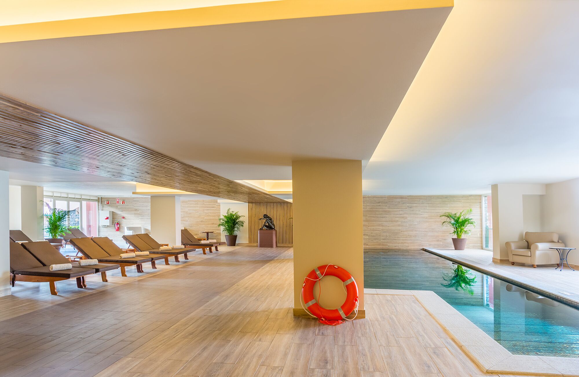 Un área de piscina interior moderna con sillones de descanso y un salvavidas.