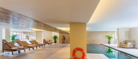 Un área de piscina interior moderna con sillones de descanso y un salvavidas.
