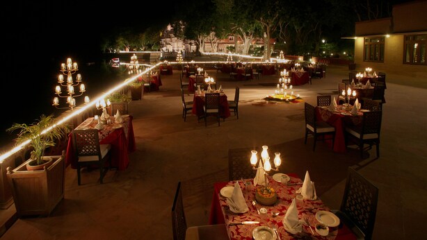 An outdoor dining area with tables set for a meal, featuring candlelight and a view of a building in the background. - Gajner Palace (Kolayat)