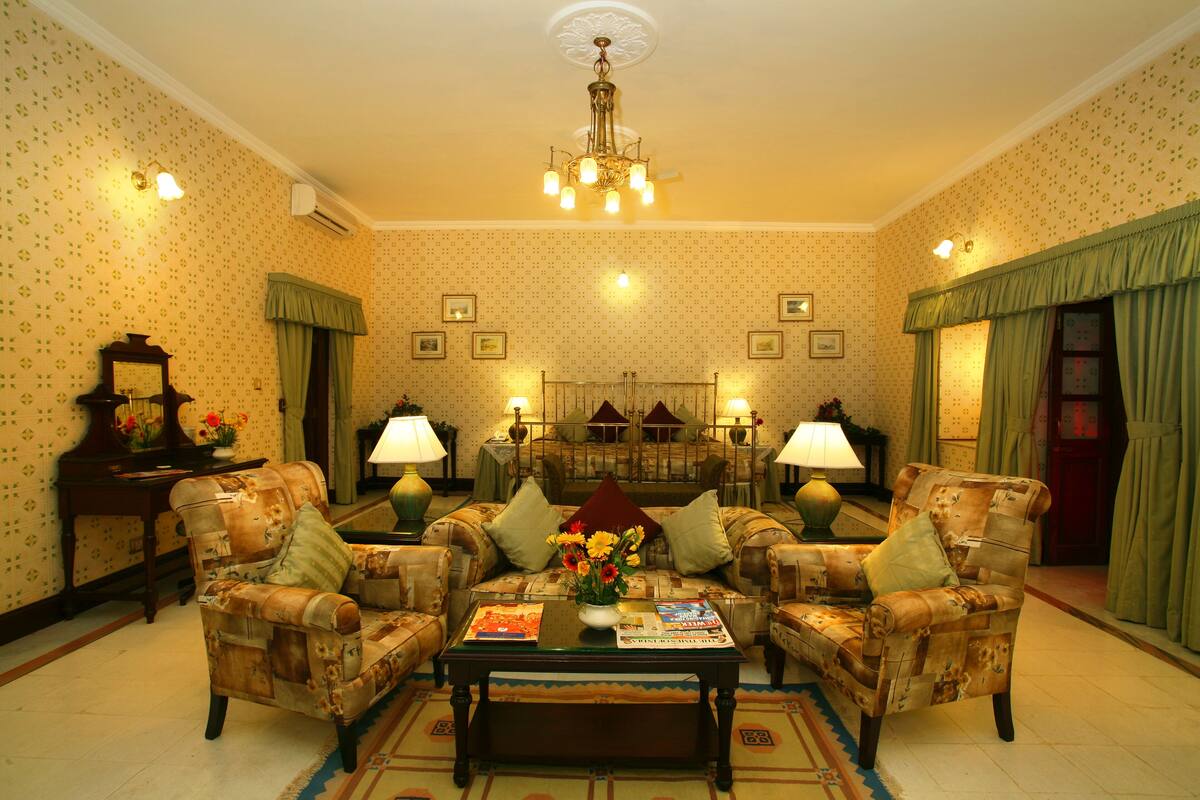 A traditional living room with patterned wallpaper, a chandelier, and two armchairs with a coffee table in the center.