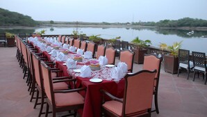 A long dining table set with white tablecloths and napkins, chairs, and a view of a calm lake. - Gajner Palace (Kolayat)