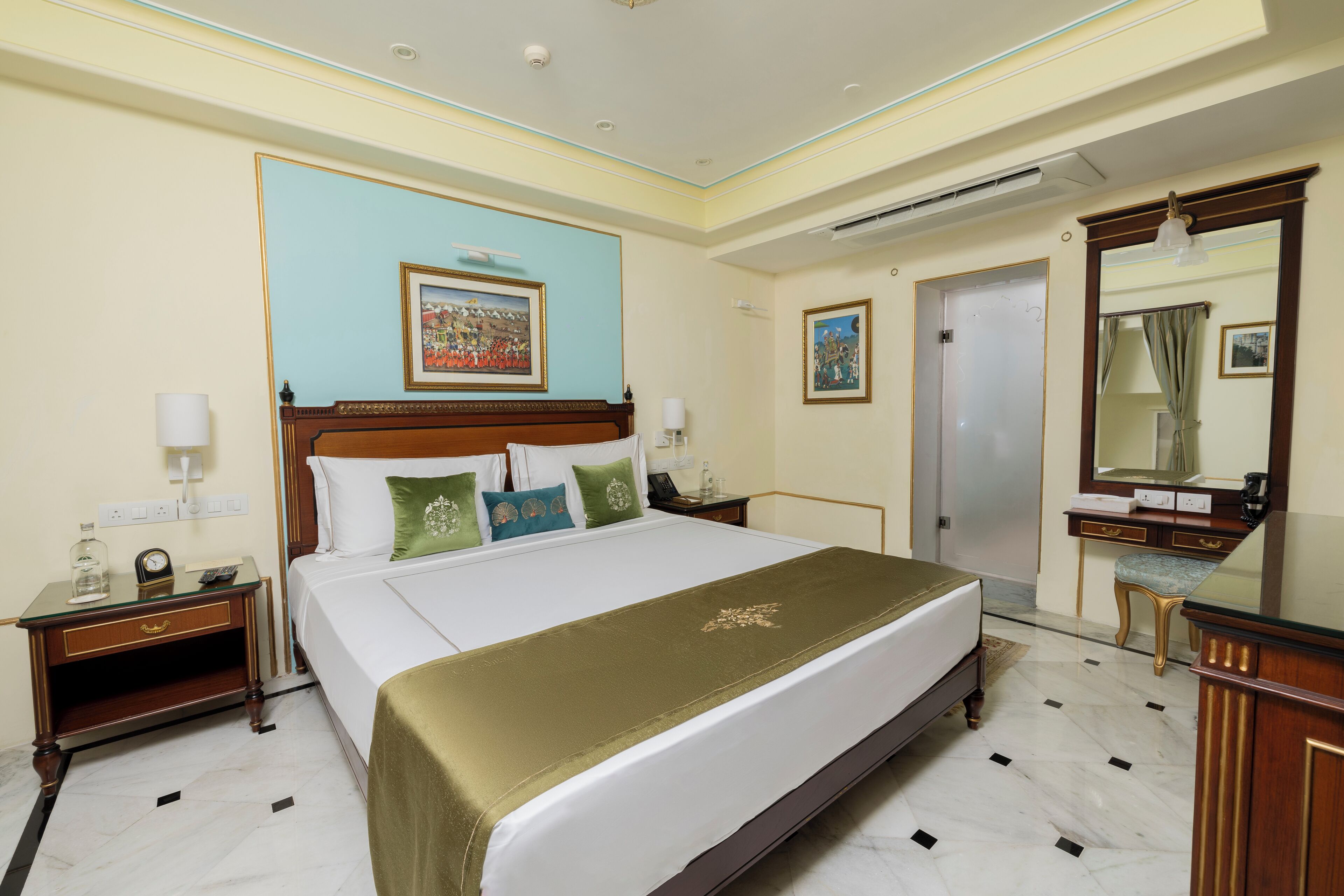 A hotel room with a large bed, a nightstand, a dresser, a mirror, and a painting on the wall.