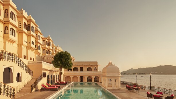 A pool area with a view of a lake and mountains, surrounded by traditional architecture with balconies and a dome structure. - Taj Fateh Prakash Palace (Udaipur)