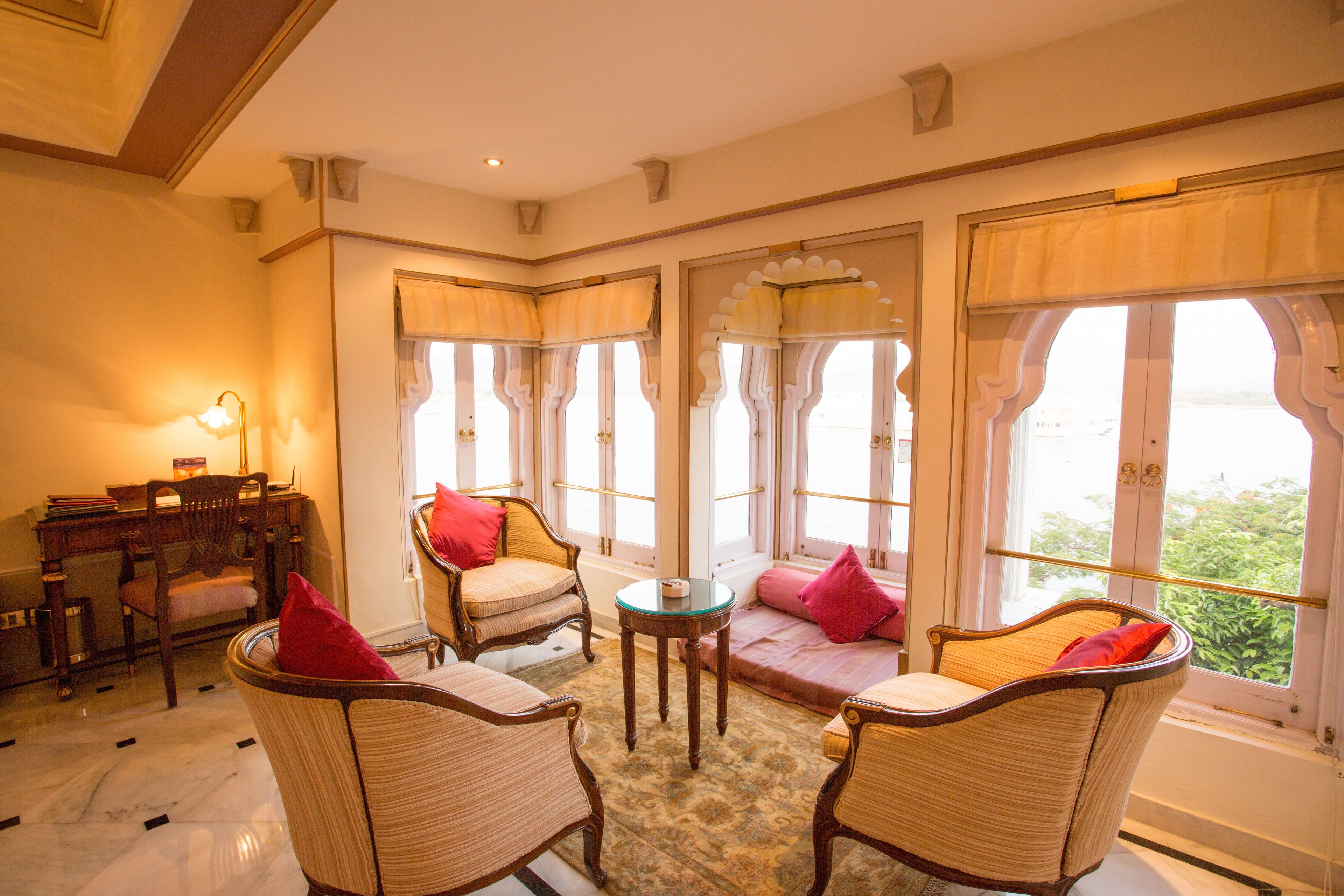 Une pièce dotée d'un coin salon avec des fauteuils en osier et une petite table, de grandes fen êtres avec des rideaux, et une vue sur la verdure à l'extérieur.