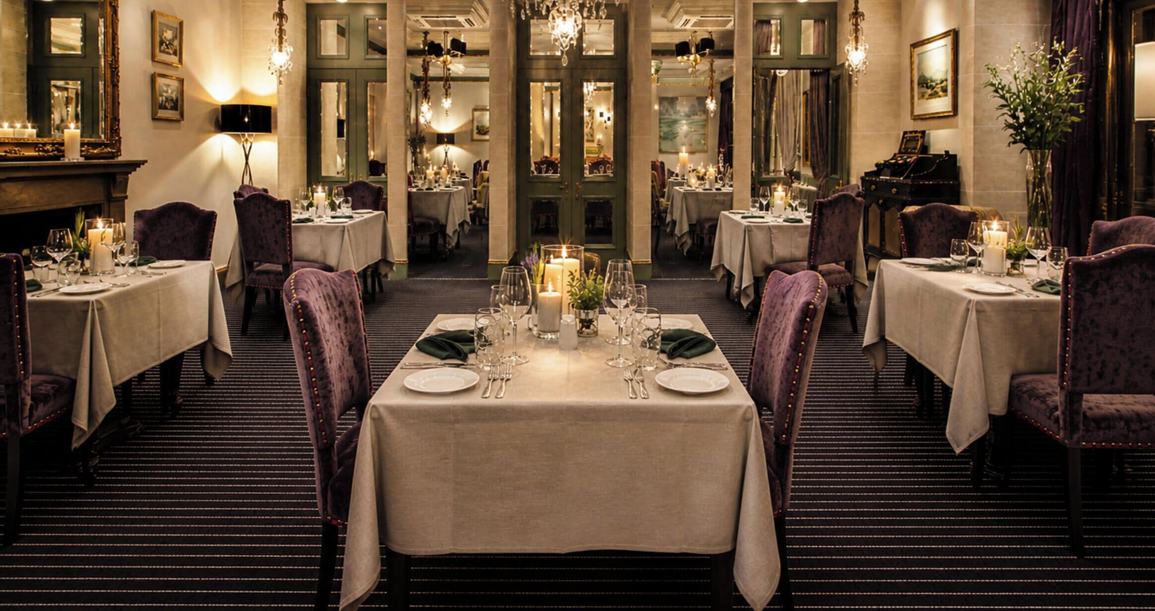 Un comedor formal con mesas dispuestas para el servicio, candelabros y obras de arte enmarcadas en las paredes.