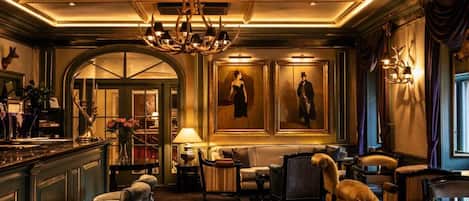 A luxurious lobby with a grand chandelier, elegant seating, and framed portraits on the walls.