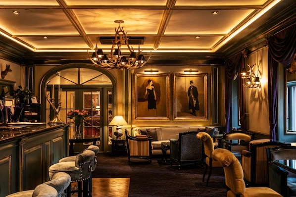 A luxurious lobby with a grand chandelier, elegant seating, and framed portraits on the walls.