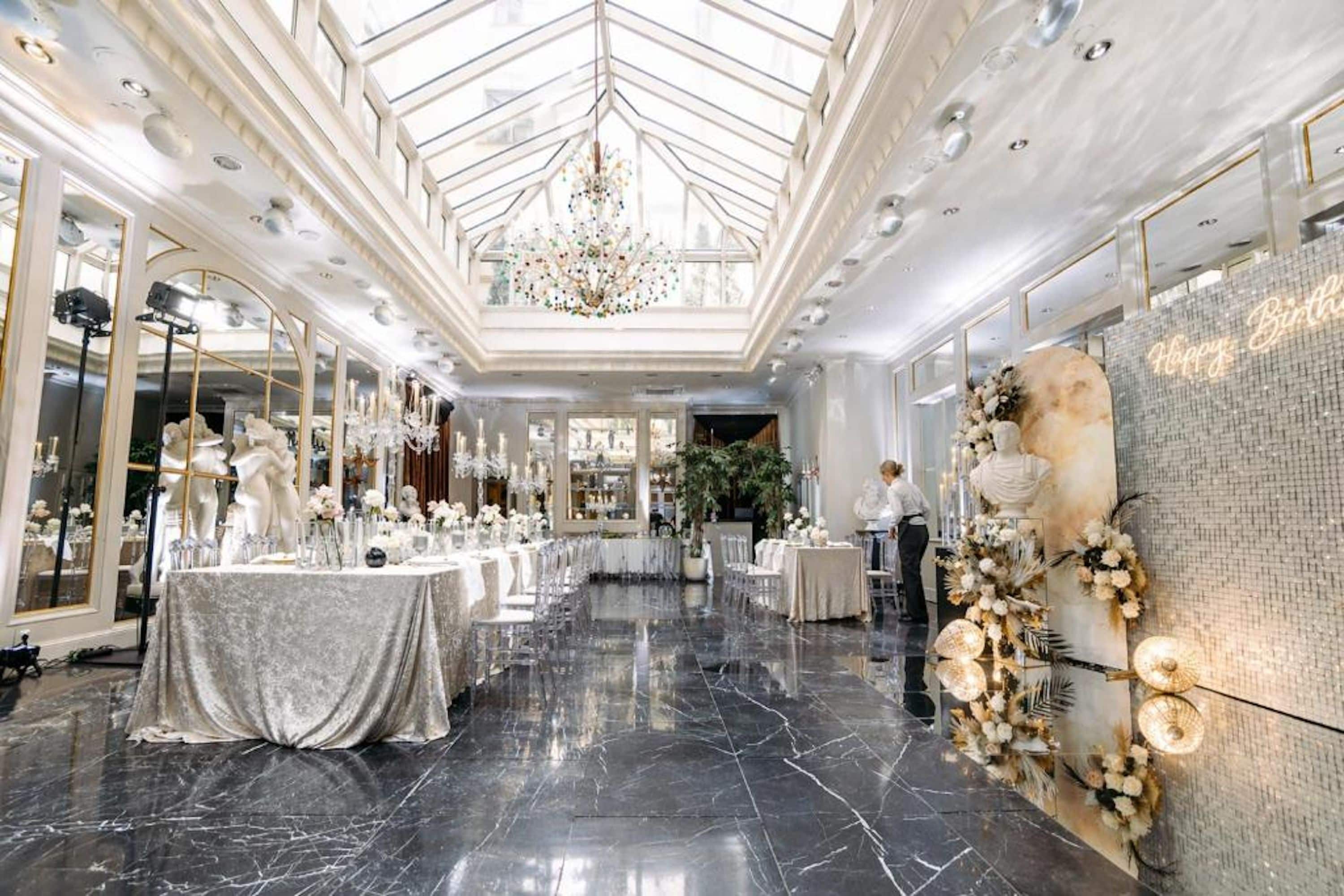 A spacious hall with a high ceiling and a central chandelier, featuring tables set for a formal event.