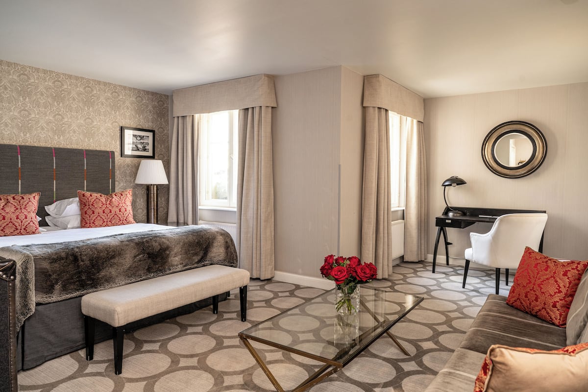 Ein Hotelzimmer mit Bett, Schreibtisch, Sofa, Bank und Couchtisch mit Blumen.