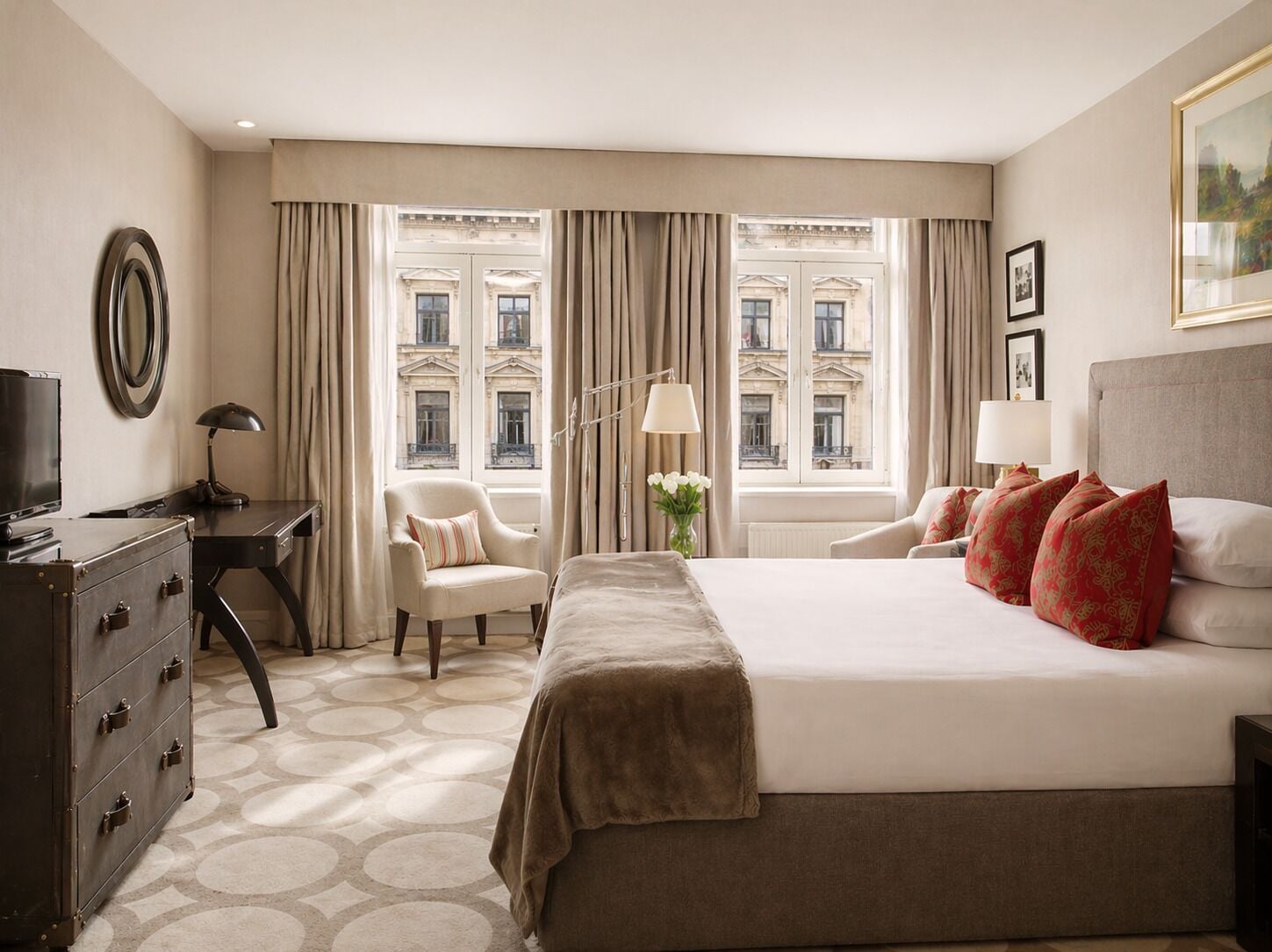 A hotel room with a large bed, a desk, a chair, a dresser, and a window with curtains.