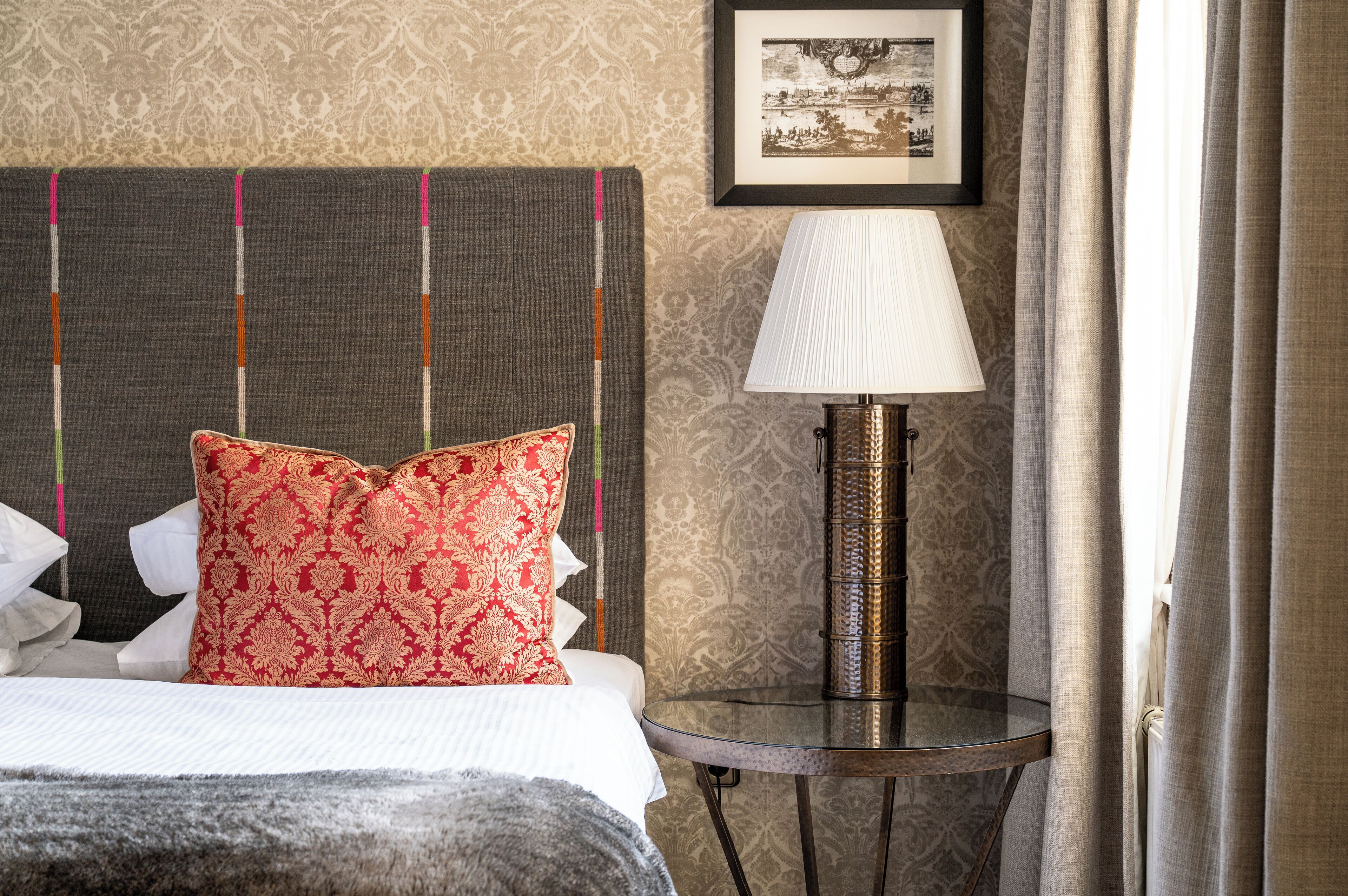 A neatly made bed with a red patterned pillow, a bedside lamp, and a framed picture on the wall.