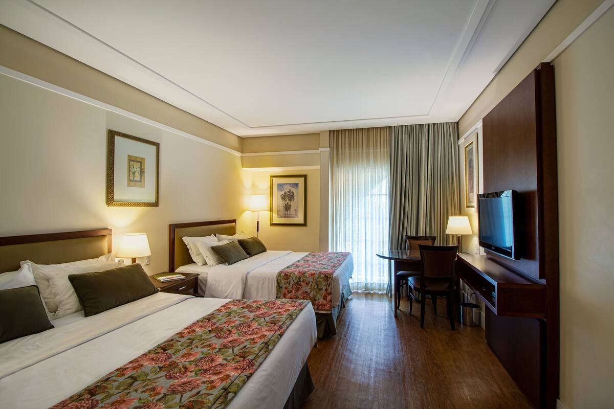 Une chambre d’hôtel avec deux lits, un bureau, une télévision et une fenêtre avec des rideaux.